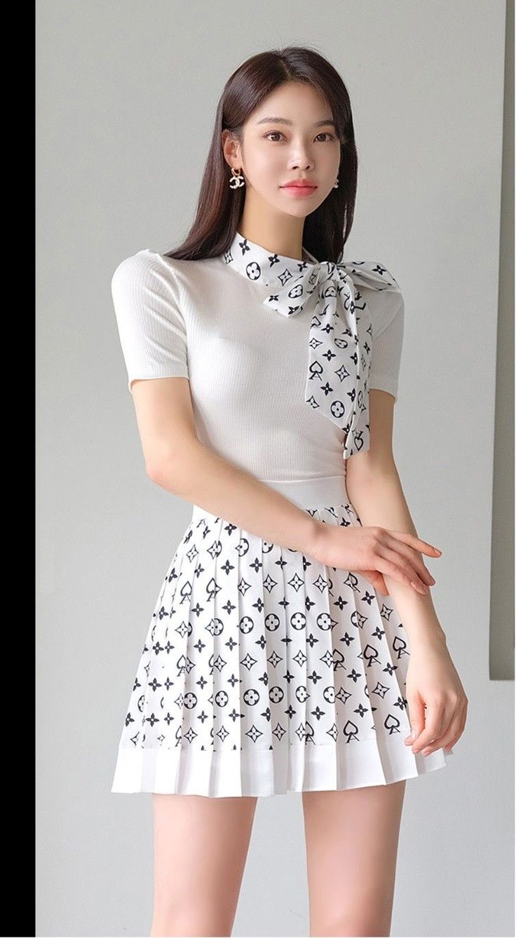 Woman with long hair wearing a white top and pleated short skirt indoors