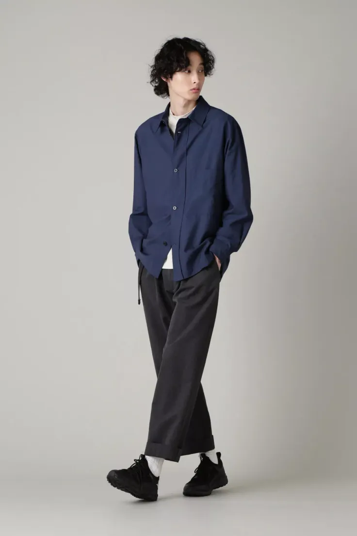 Man in a navy blue shirt and black pants with curly hair in a studio
