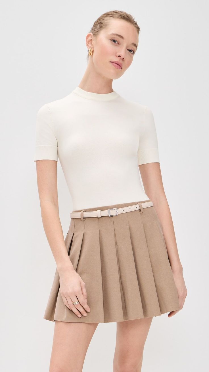 Woman in a cream short-sleeve top and a pleated brown skirt