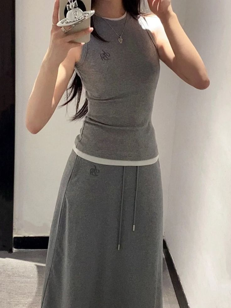 Person in a gray tank top and midi skirt taking a mirror selfie