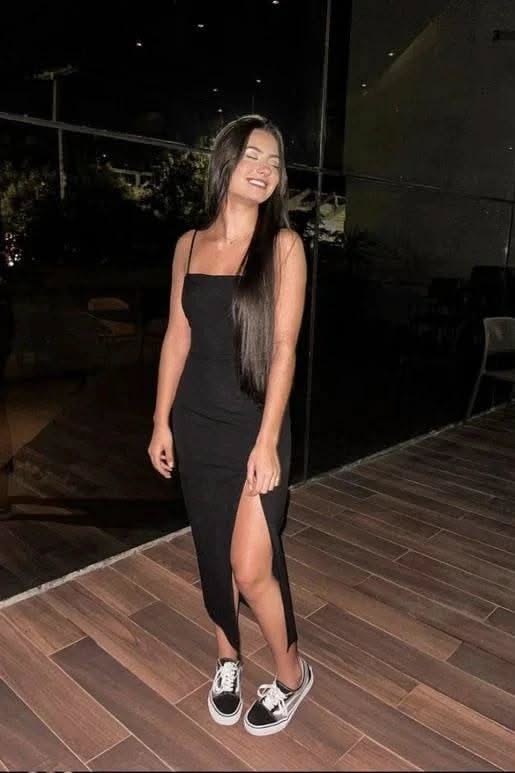 Woman in a black dress with a high slit and sneakers at night