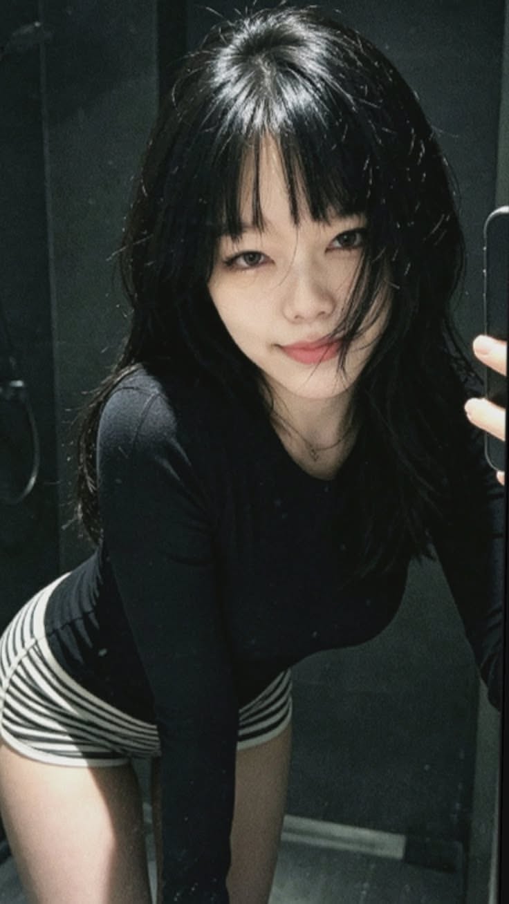 Woman with long black hair and bangs in a black long sleeve shirt and striped shorts