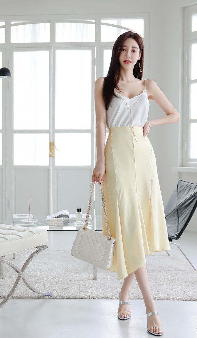 Woman in a white camisole and yellow skirt holding a quilted handbag indoors