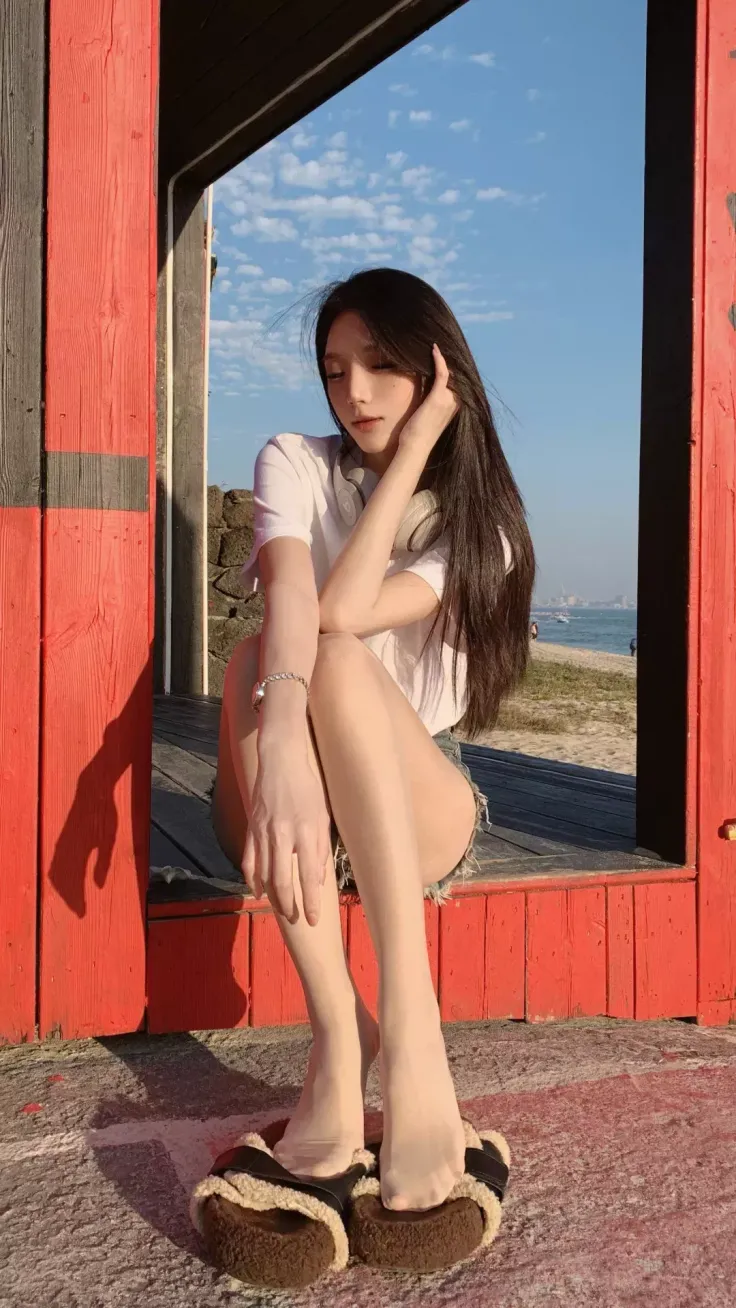 Woman with long hair and headphones sitting in a red frame at the beach
