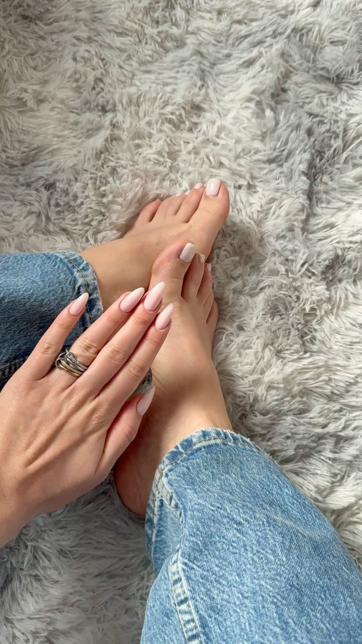Hand with light pink nails and rings touching feet on a fluffy rug