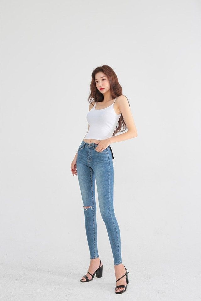 Woman in a white tank top and skinny jeans posing against a white background