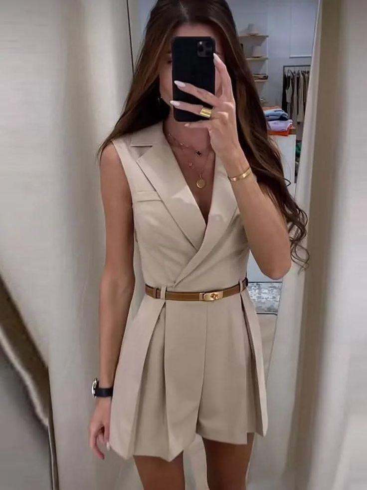 Woman in a sleeveless blazer dress and brown belt taking a mirror selfie