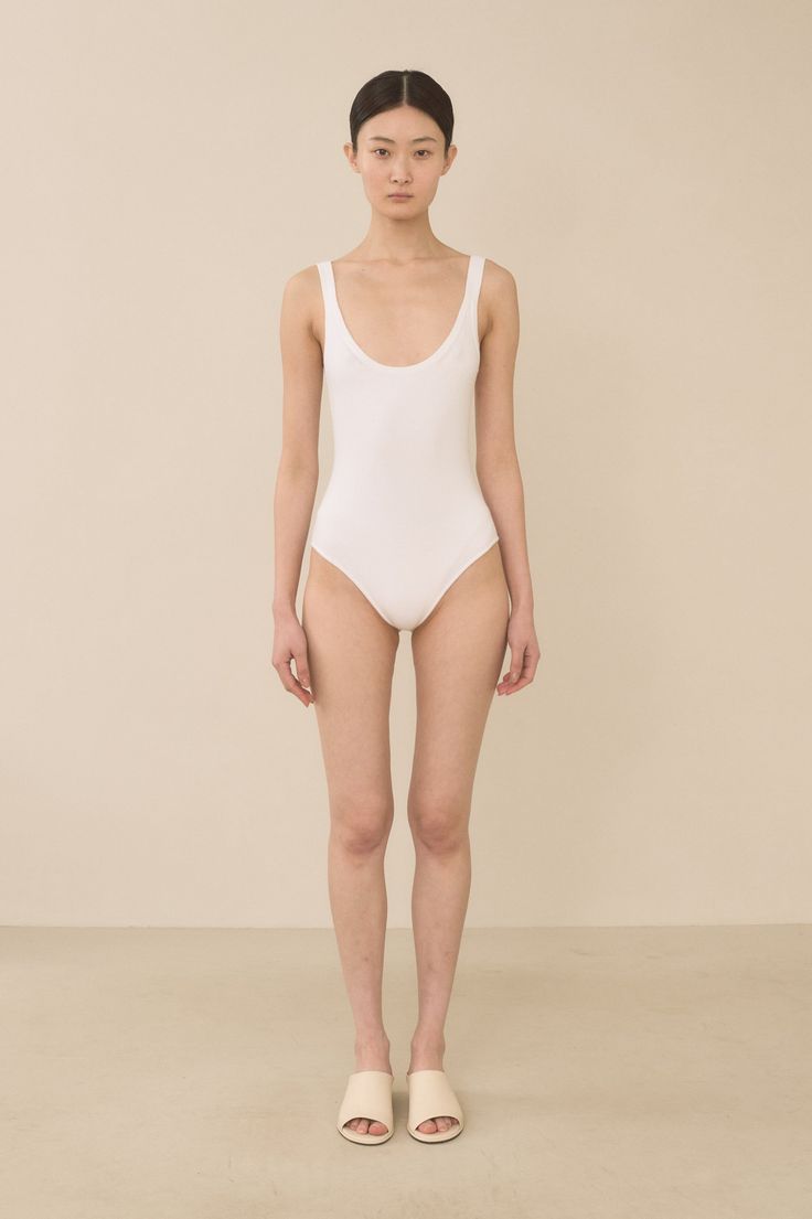Woman in a white swimsuit standing against a plain background