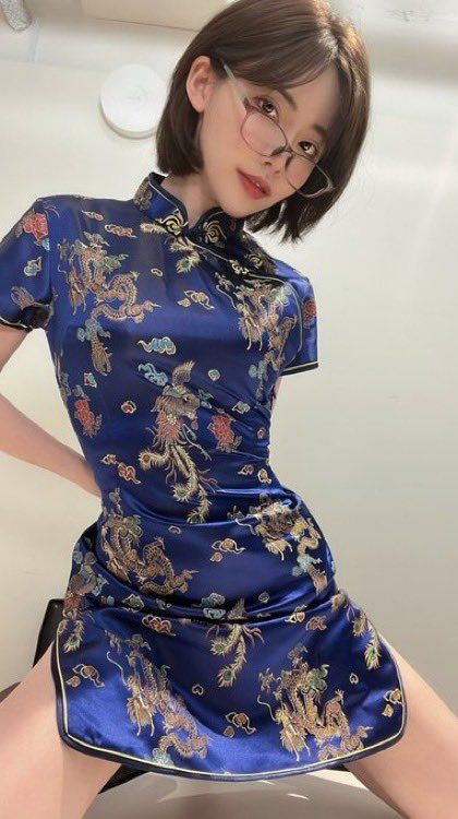 Woman in a blue cheongsam with dragon patterns and glasses posing indoors