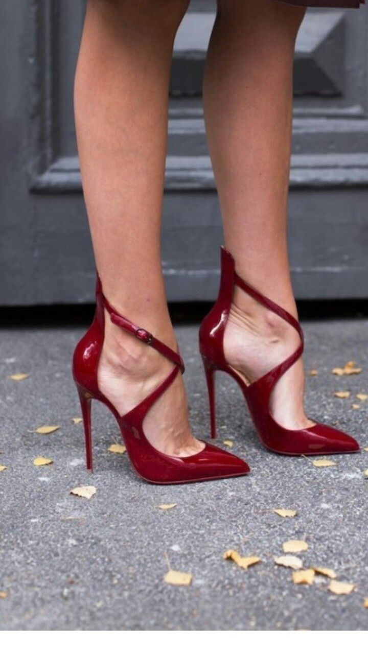 Woman's legs in red strappy high heels on a paved surface with fallen leaves
