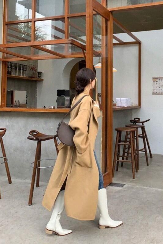 Woman in a long tan coat and white boots walking through a cafe