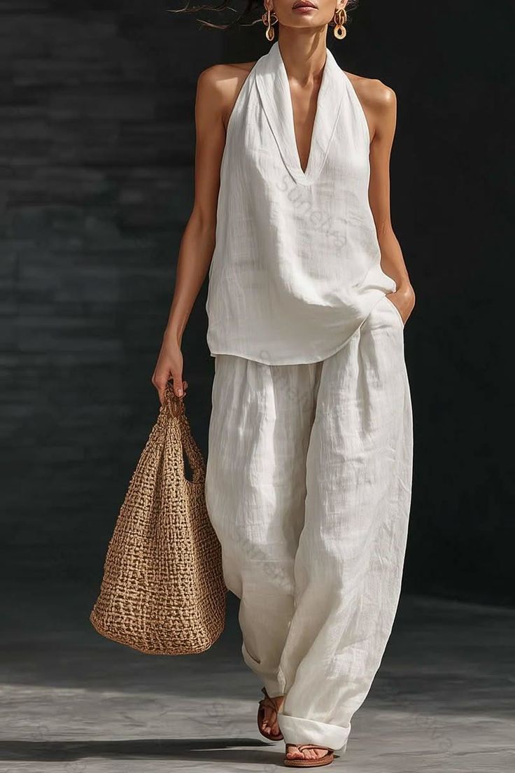 Woman in a white linen halter top and wide leg pants holding a straw bag