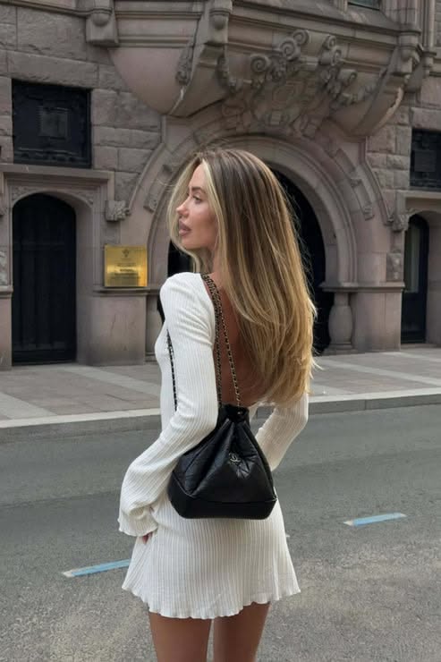Woman with long hair in a white open-back dress and black handbag on a street
