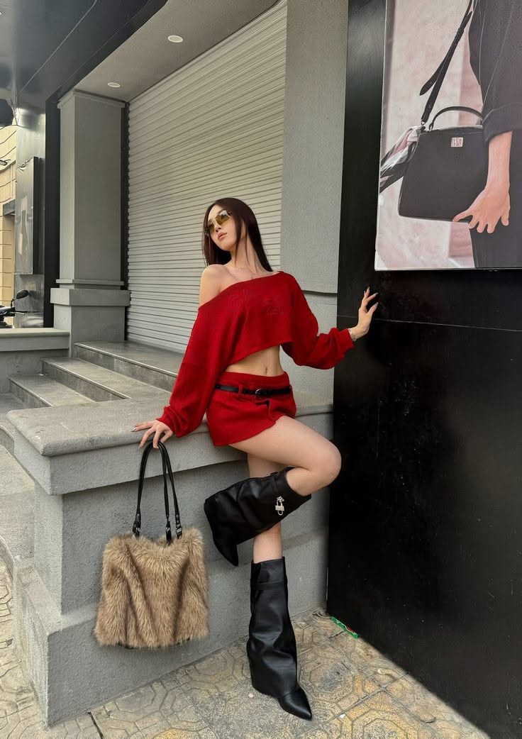 Woman in a red crop top and mini skirt with black boots and a furry bag