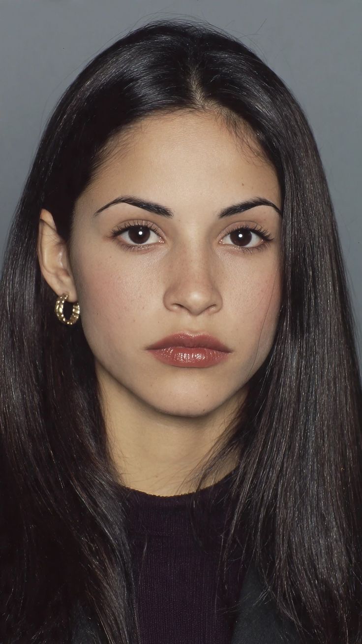 Woman with long dark hair and gold earrings looking directly at the camera