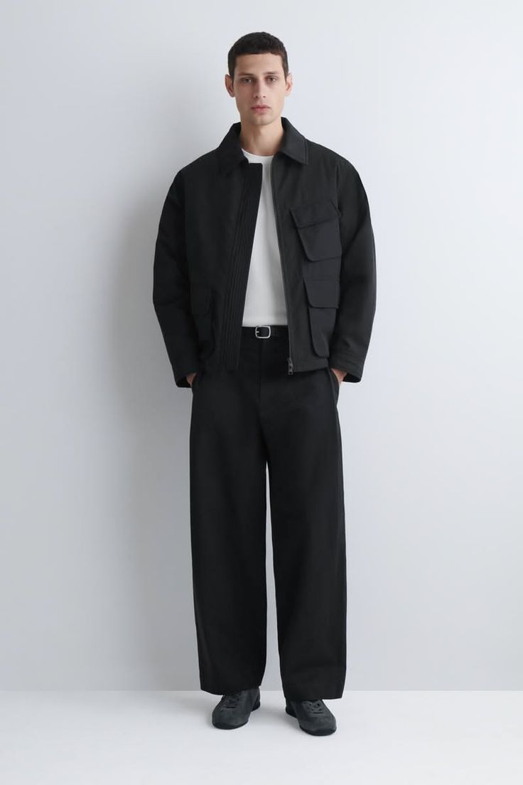 Man in a black jacket and wide leg pants standing against a white background