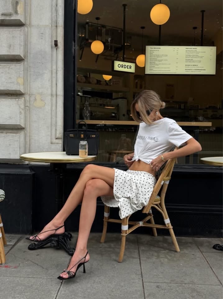 Woman in a polka dot skirt and knotted t-shirt sitting at an outdoor cafe