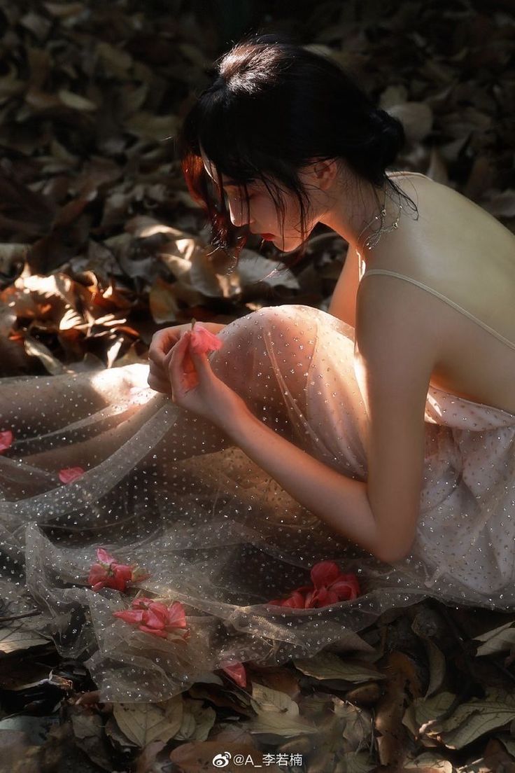 Woman in a sparkly dress with an exposed back, holding a flower among fallen leaves