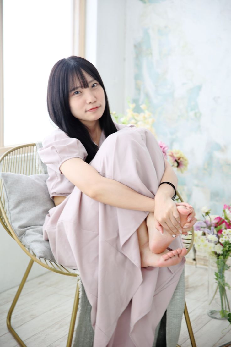 Woman with long black hair in a light pink dress sitting indoors