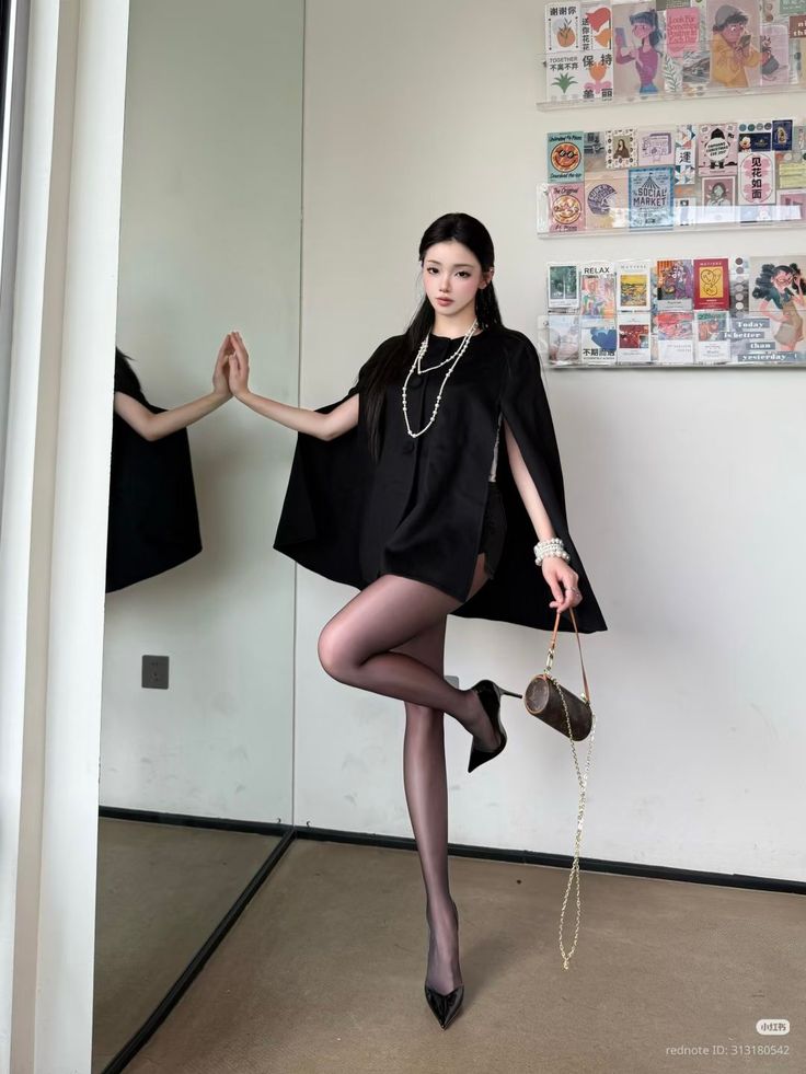 Woman in a black cape and pantyhose posing indoors with a mirror