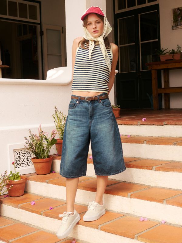 Woman in a striped top, denim culottes, and red cap standing on terracotta steps