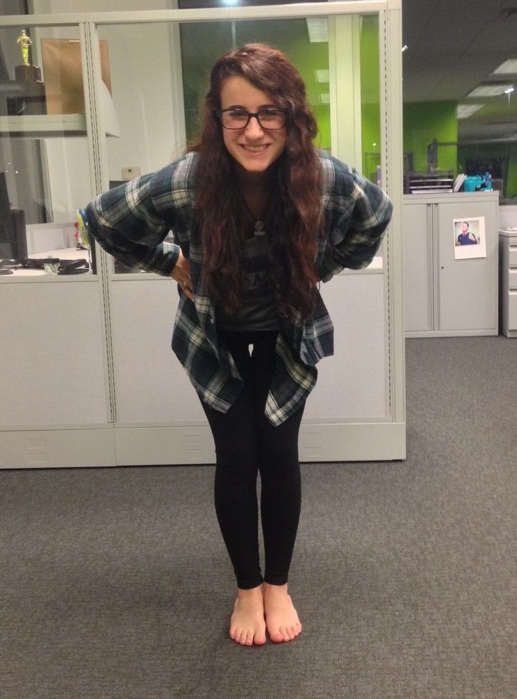 Woman with long hair and glasses wearing a plaid shirt and leggings, smiling in an office