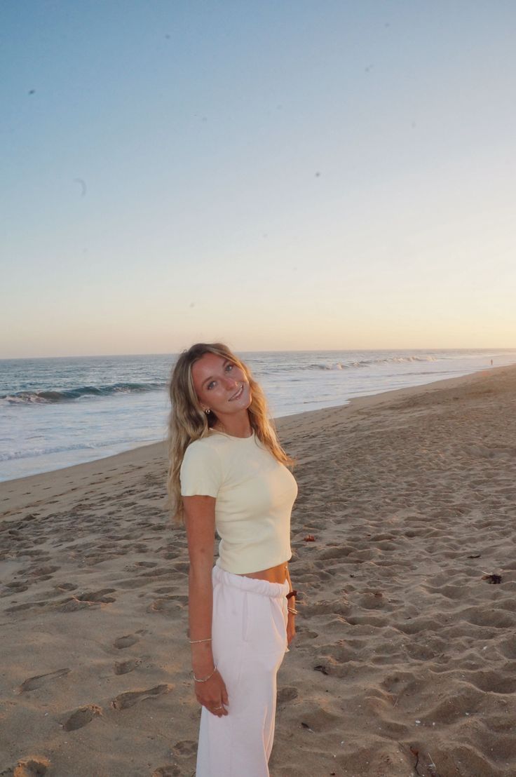 Woman with long hair on a beach at sunset wearing a crop top and sweatpants