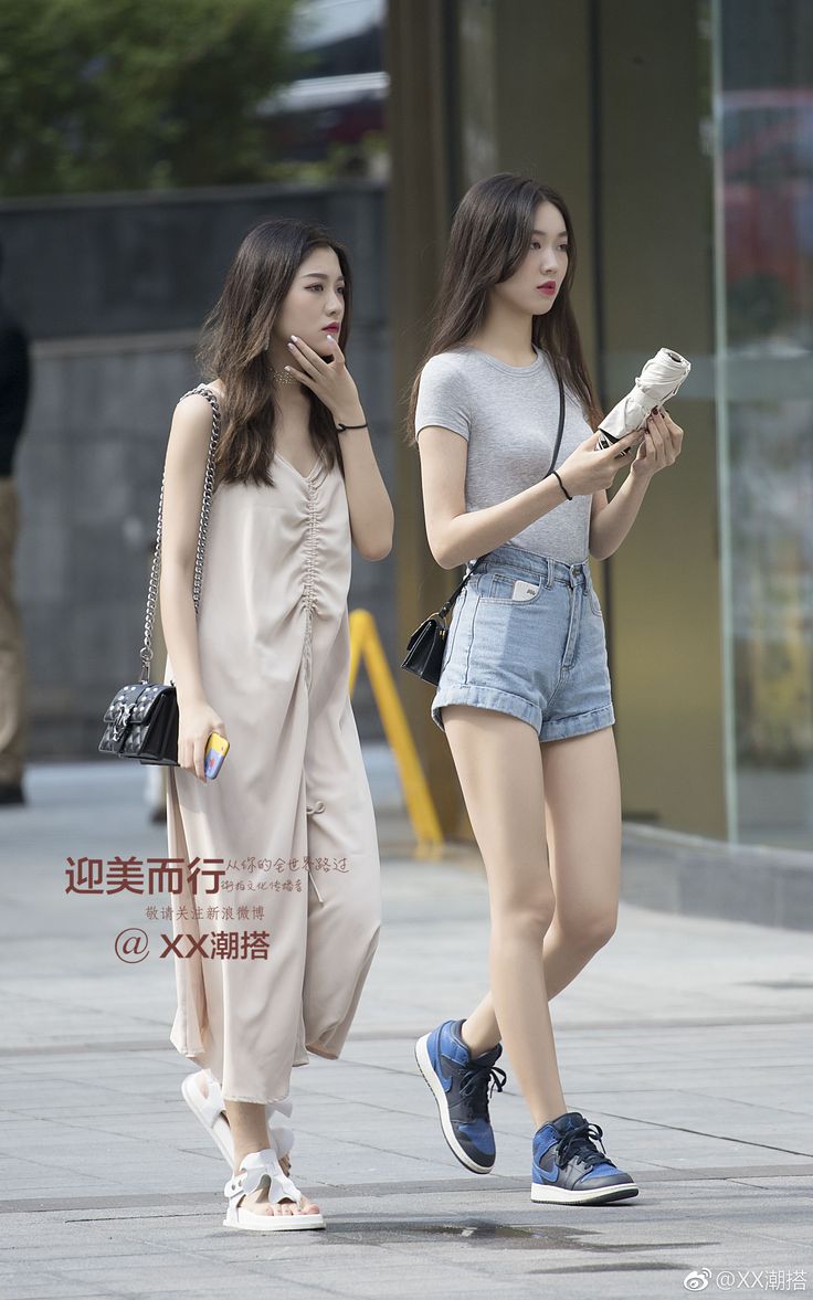 Two women walking on a street, one in a jumpsuit and the other in denim shorts