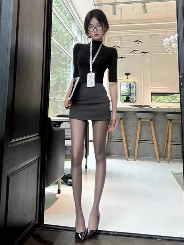 Woman in a black turtleneck, mini skirt, and sheer pantyhose standing indoors