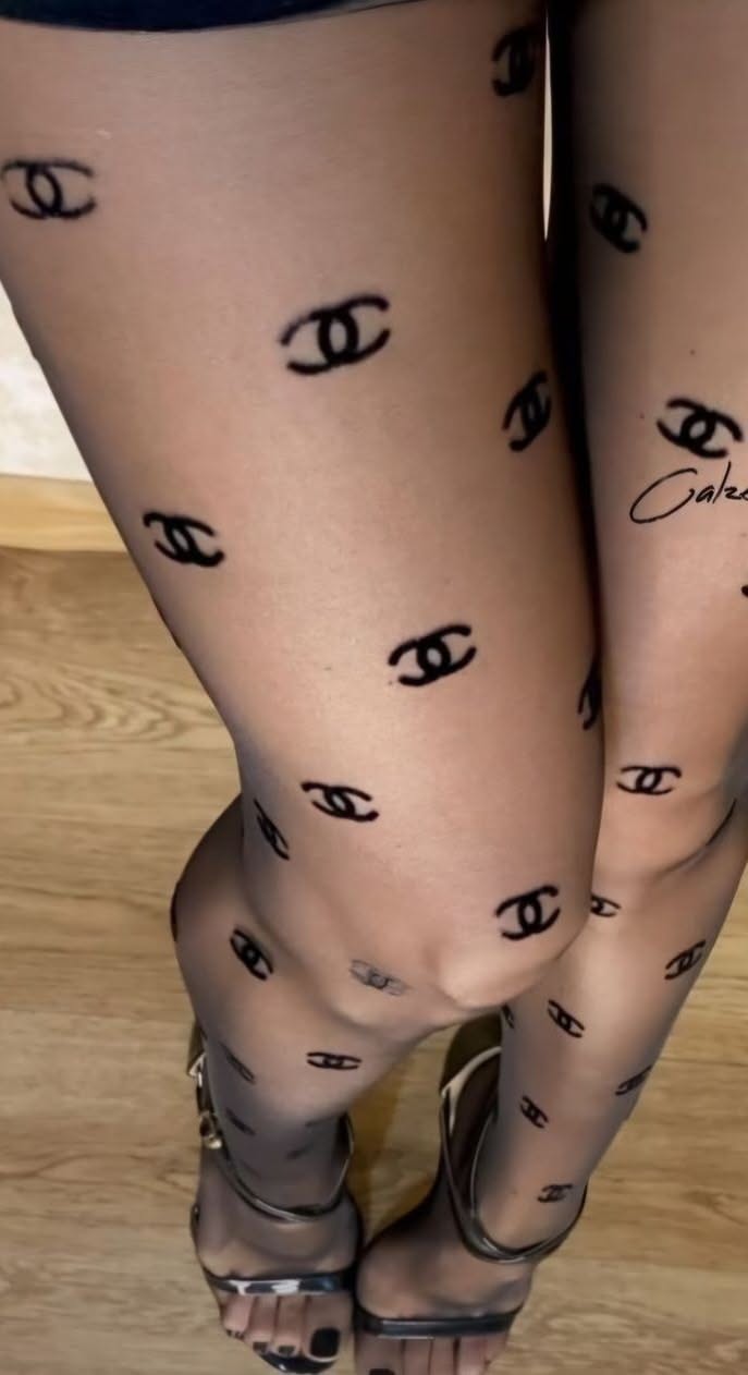 Legs in black tights with Chanel logos and high heels on a wooden floor