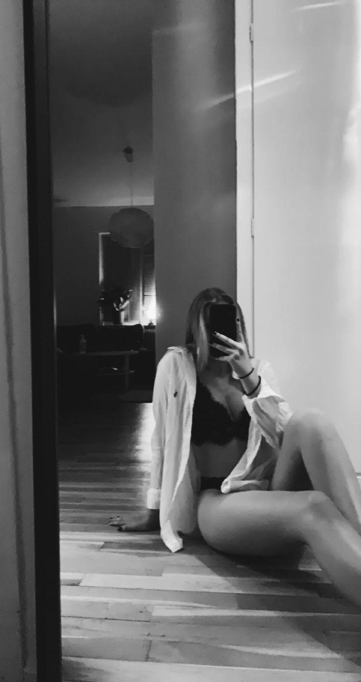 Woman in lingerie and an open white shirt taking a mirror selfie