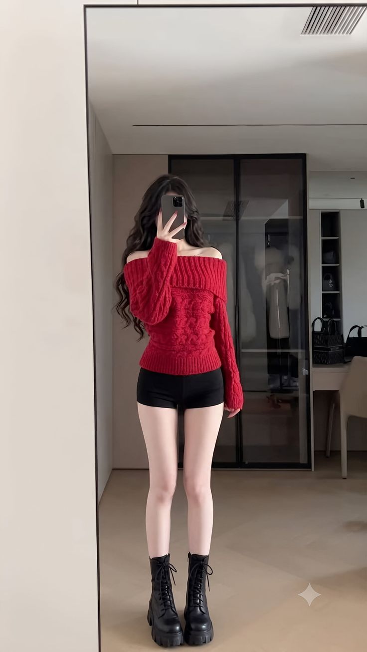 Woman in a red off-shoulder sweater and black shorts taking a mirror selfie
