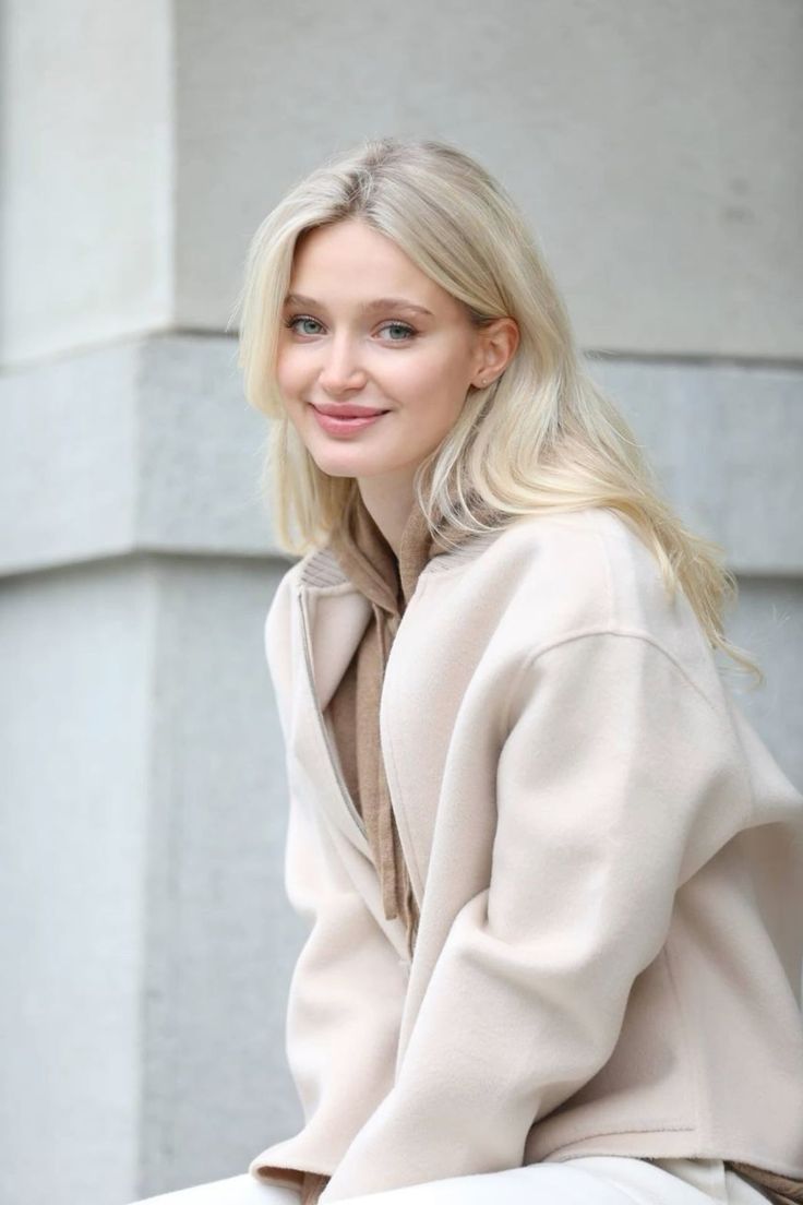 Blonde woman in a beige jacket and hoodie smiling outdoors
