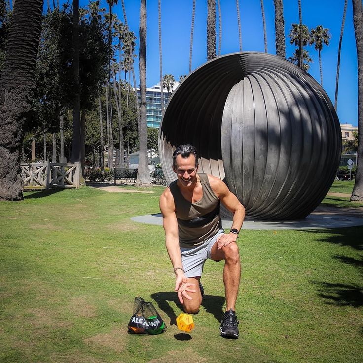 Man kneeling on grass in a park with palm trees and a large sculpture