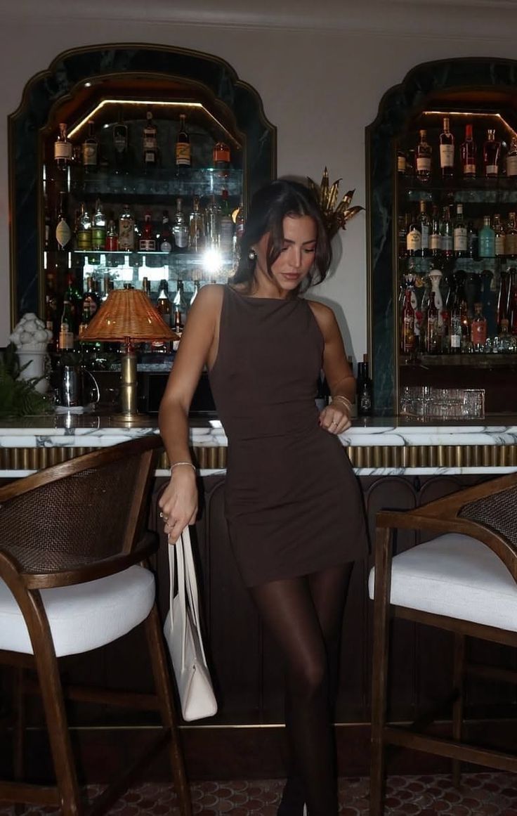 Woman in a dark mini dress and black tights leaning on a bar counter