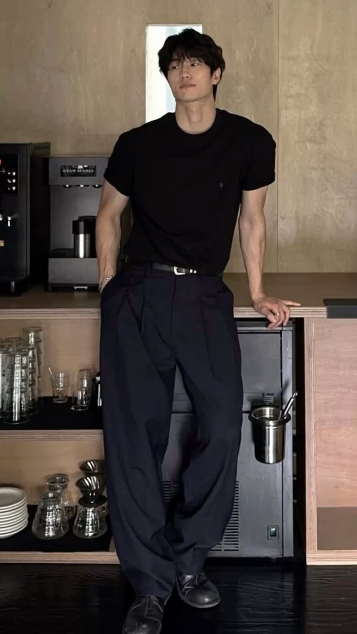 Man in a black t-shirt and dark pants leaning on a counter in a coffee shop
