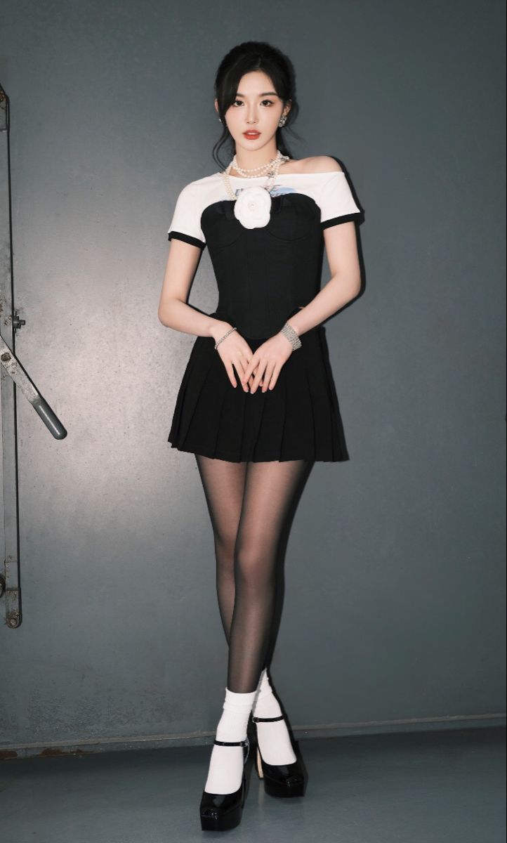 Woman in a black dress with a pleated skirt and pearl necklace standing indoors