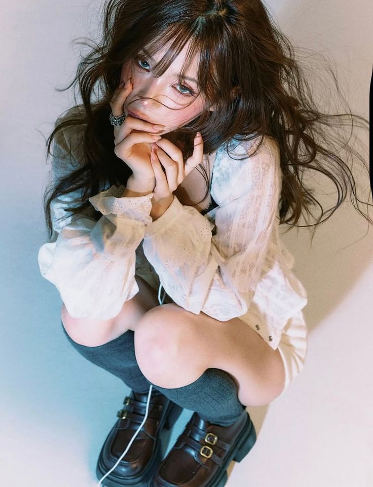 Woman with long hair in a white blouse and dark socks squatting indoors