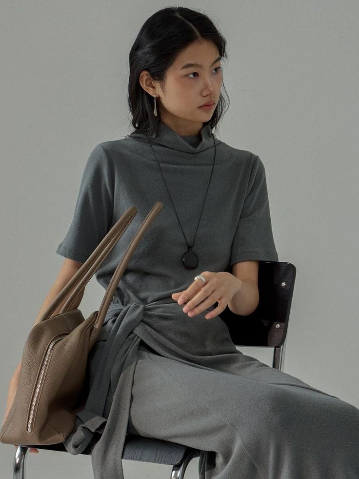 Woman in a gray turtleneck dress with a brown bag, sitting indoors