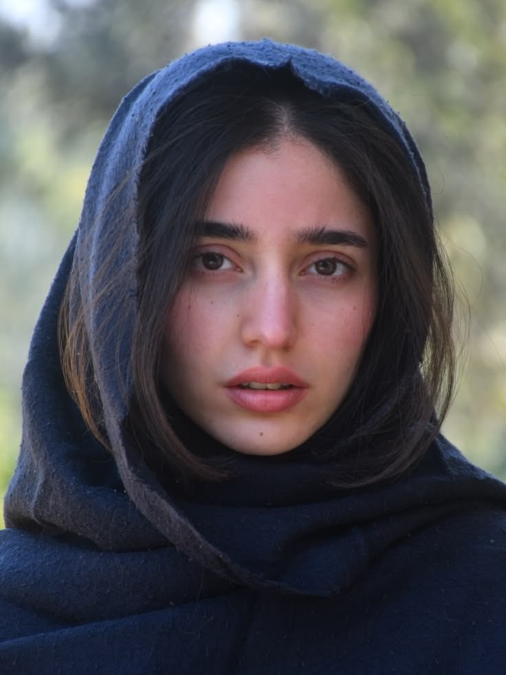 Woman with dark hair wearing a dark hood outdoors