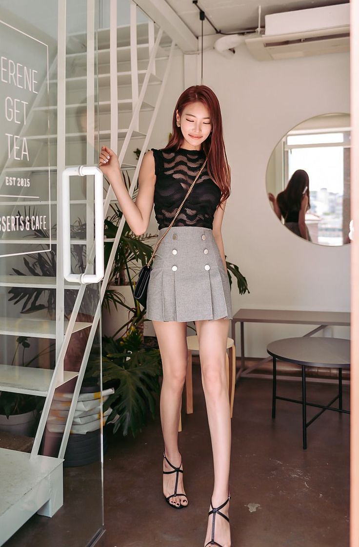 Woman in a sheer black top and grey mini skirt walking indoors