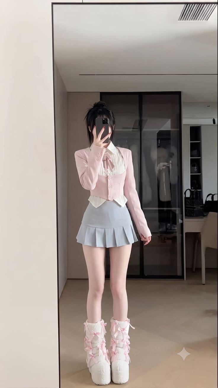 Person in a pink jacket and pleated skirt taking a mirror selfie