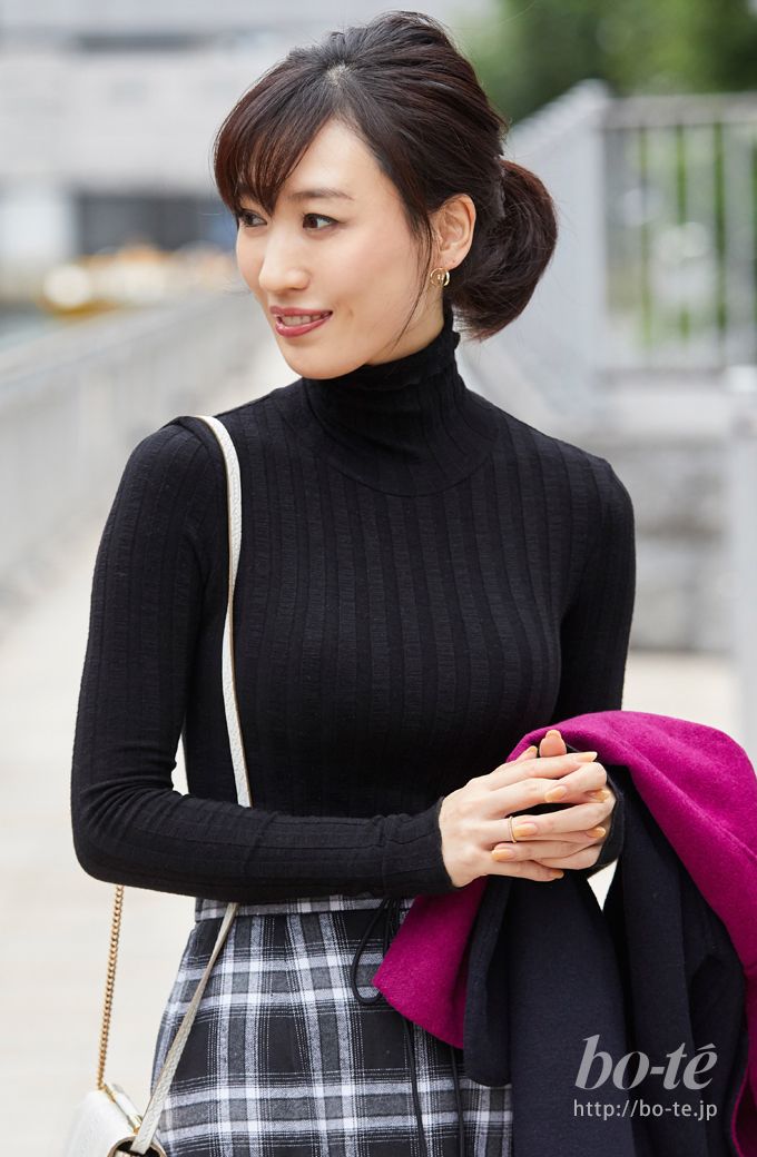 Woman in a black turtleneck and plaid skirt holding a magenta coat outdoors