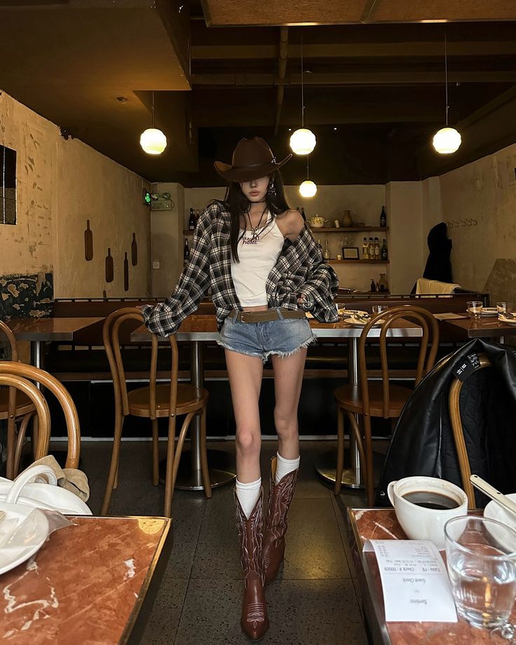 Woman in a cowboy hat, plaid shirt, and denim shorts in an indoor setting