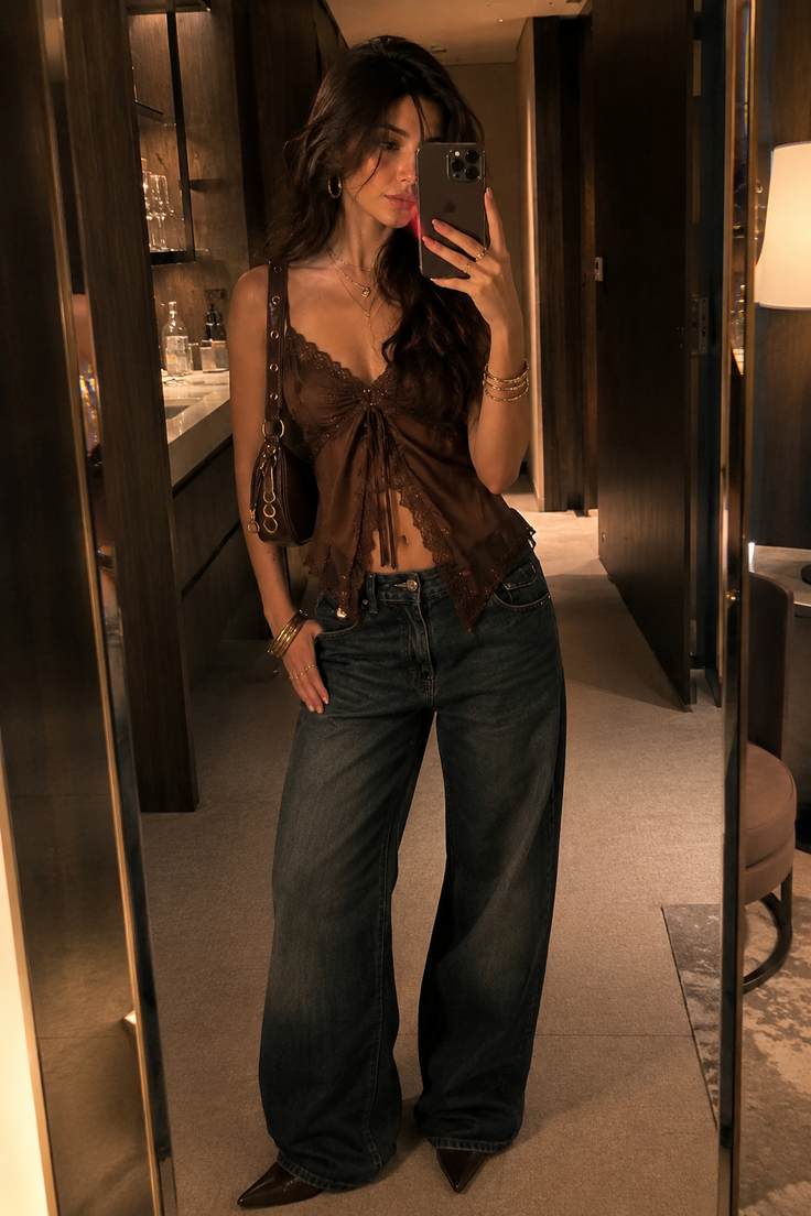 Woman in a brown lace top and wide leg jeans taking a mirror selfie indoors