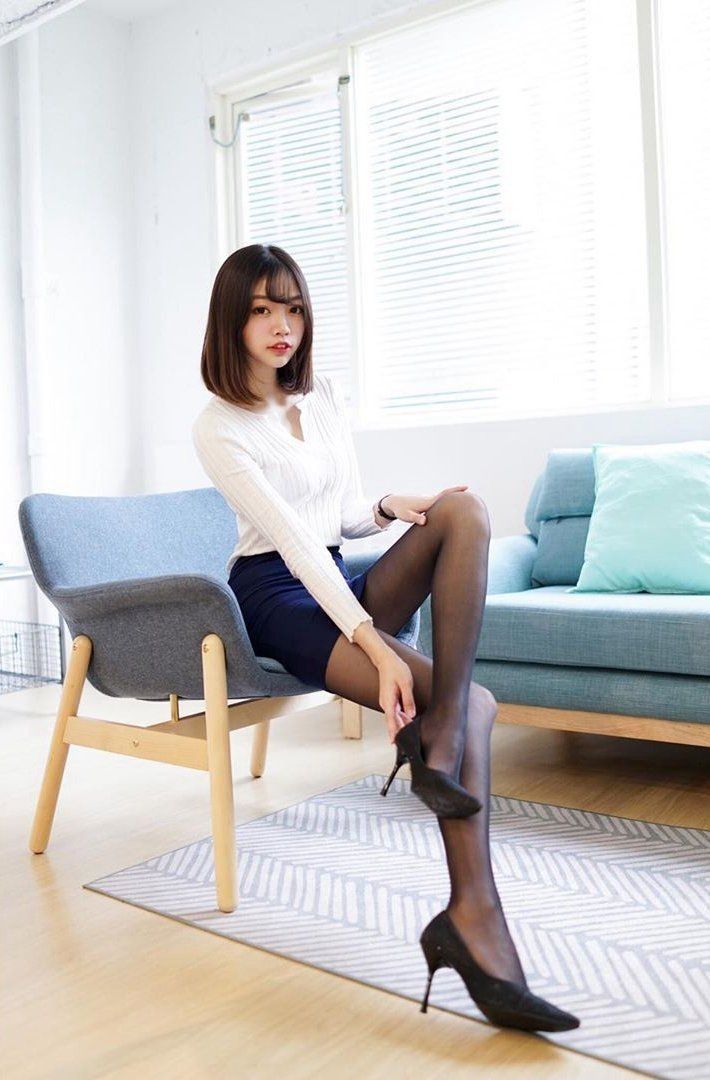 Woman in a white top, black mini skirt, and pantyhose sitting indoors