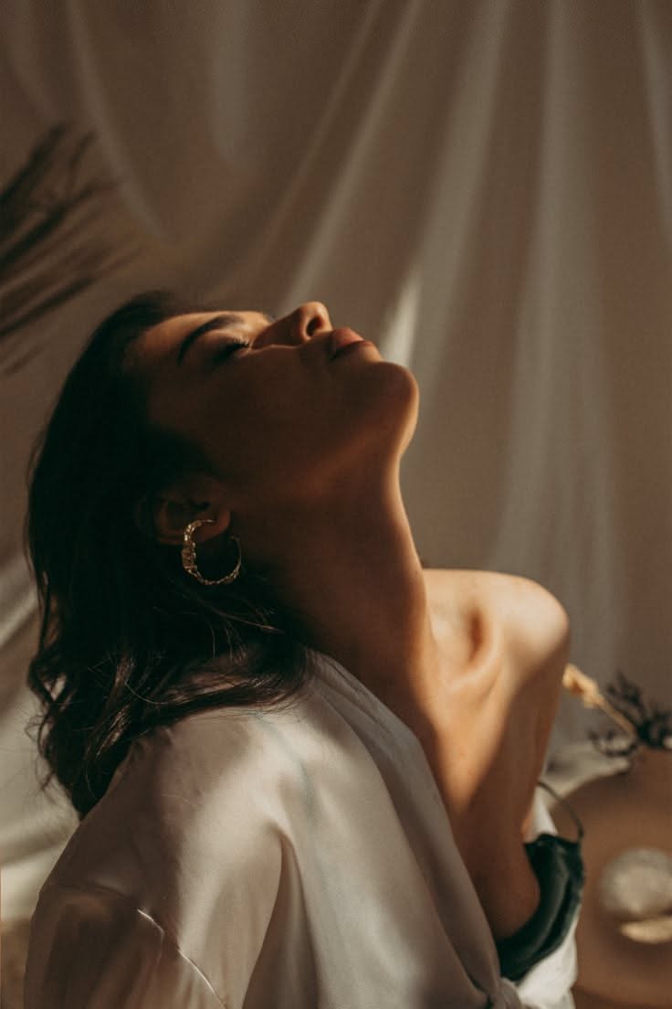 Woman with long hair and gold earrings, head tilted back in soft, dramatic lighting