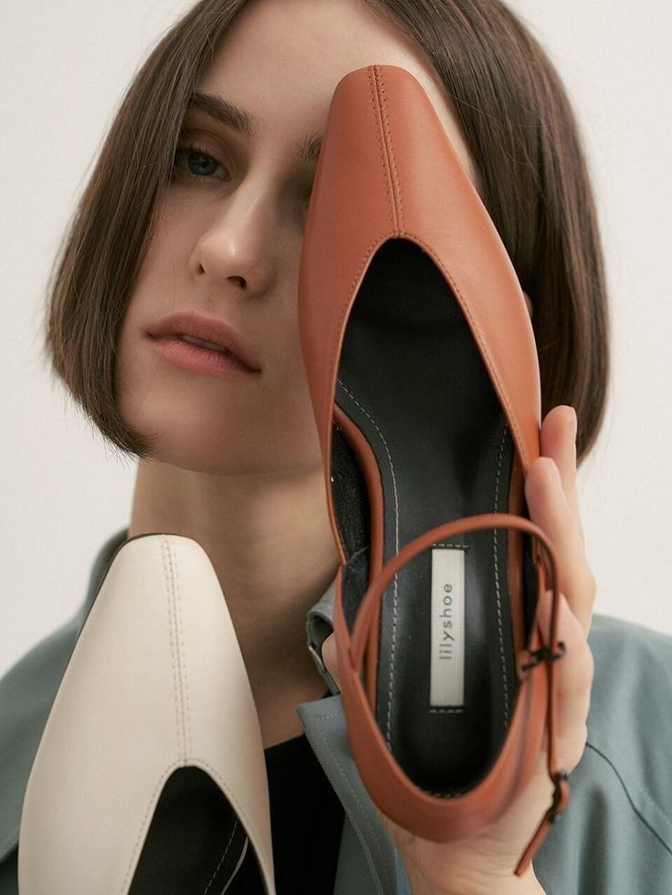Woman with short brown hair holding two pointed-toe shoes