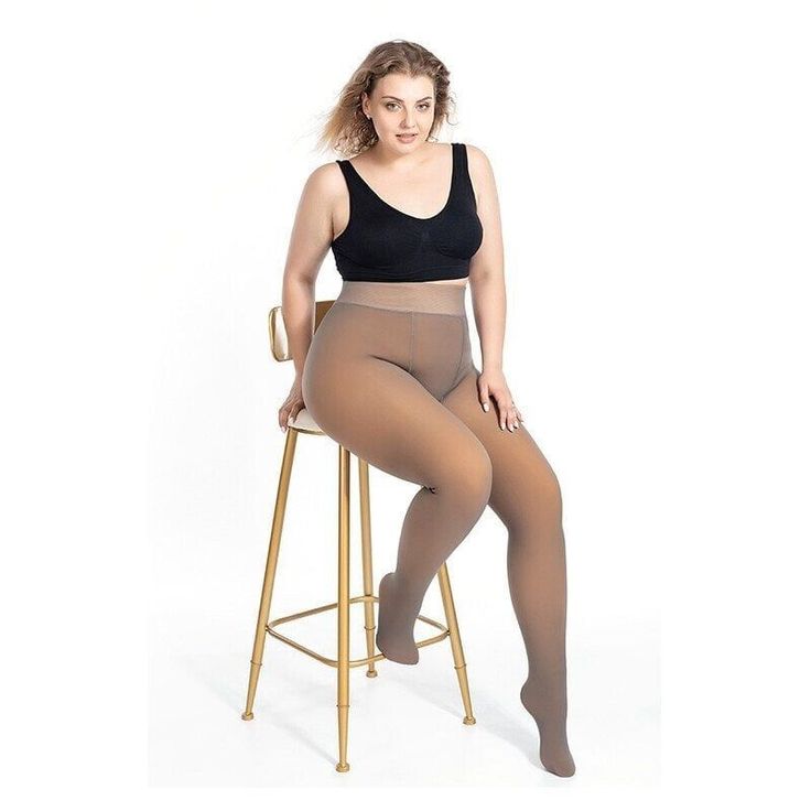 Woman with a curvy body wearing a black bra and tights, sitting on a stool