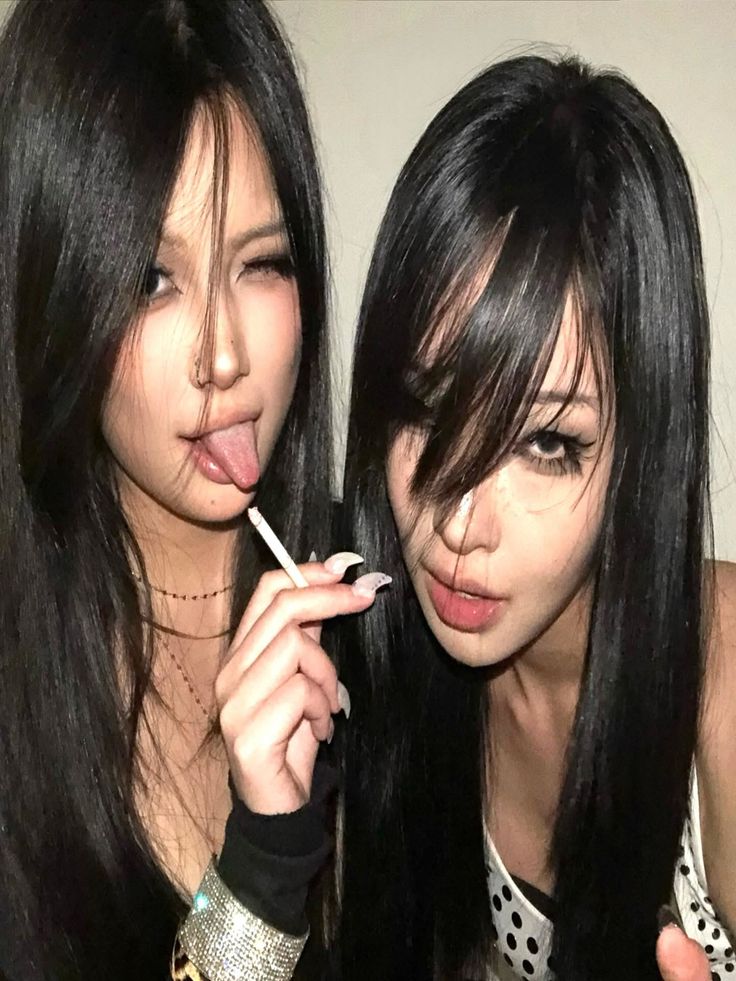 Two women with long black hair, one winking with tongue out and holding a cigarette
